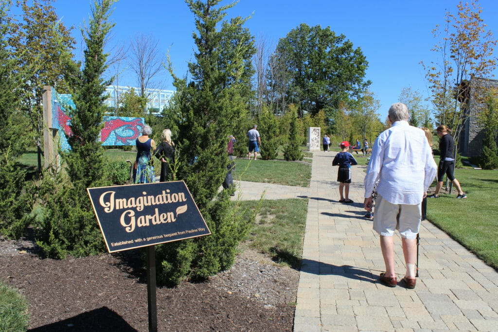 the Imagination Garden sign on a sunny day, as people walk through the garden