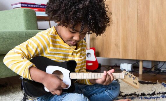 Kid-sitting and holding a Loog Guitar
